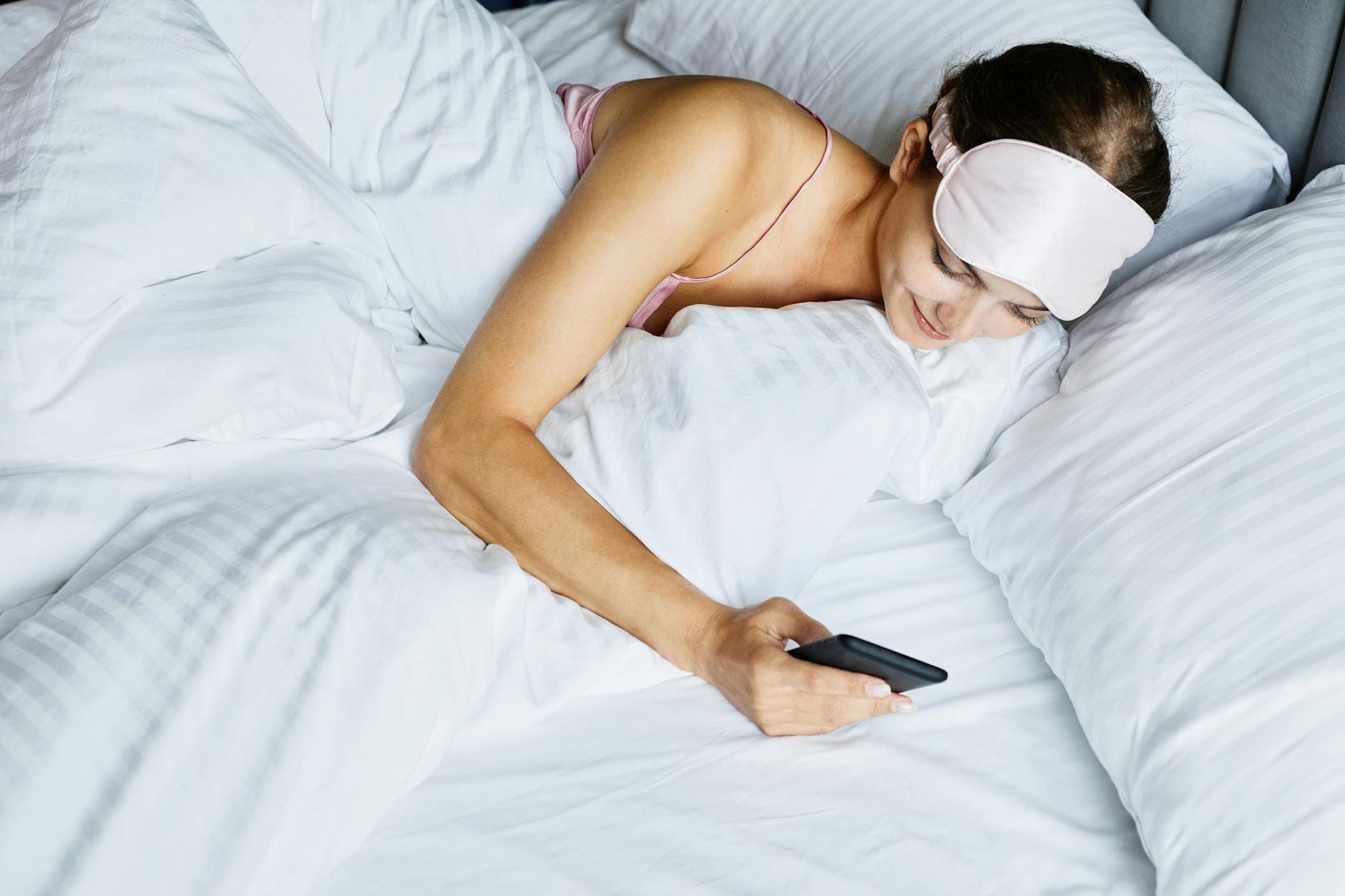 Kobieta w opasce na oczy leży w łóżku i przegląda telefon