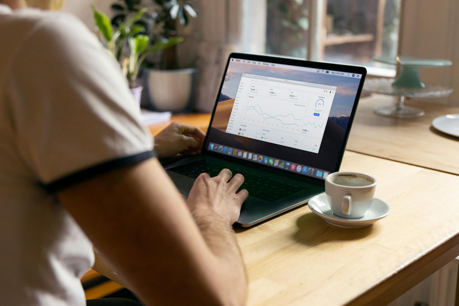 Osoba z kawą pracująca na laptopie z wykresami w domowym biurze