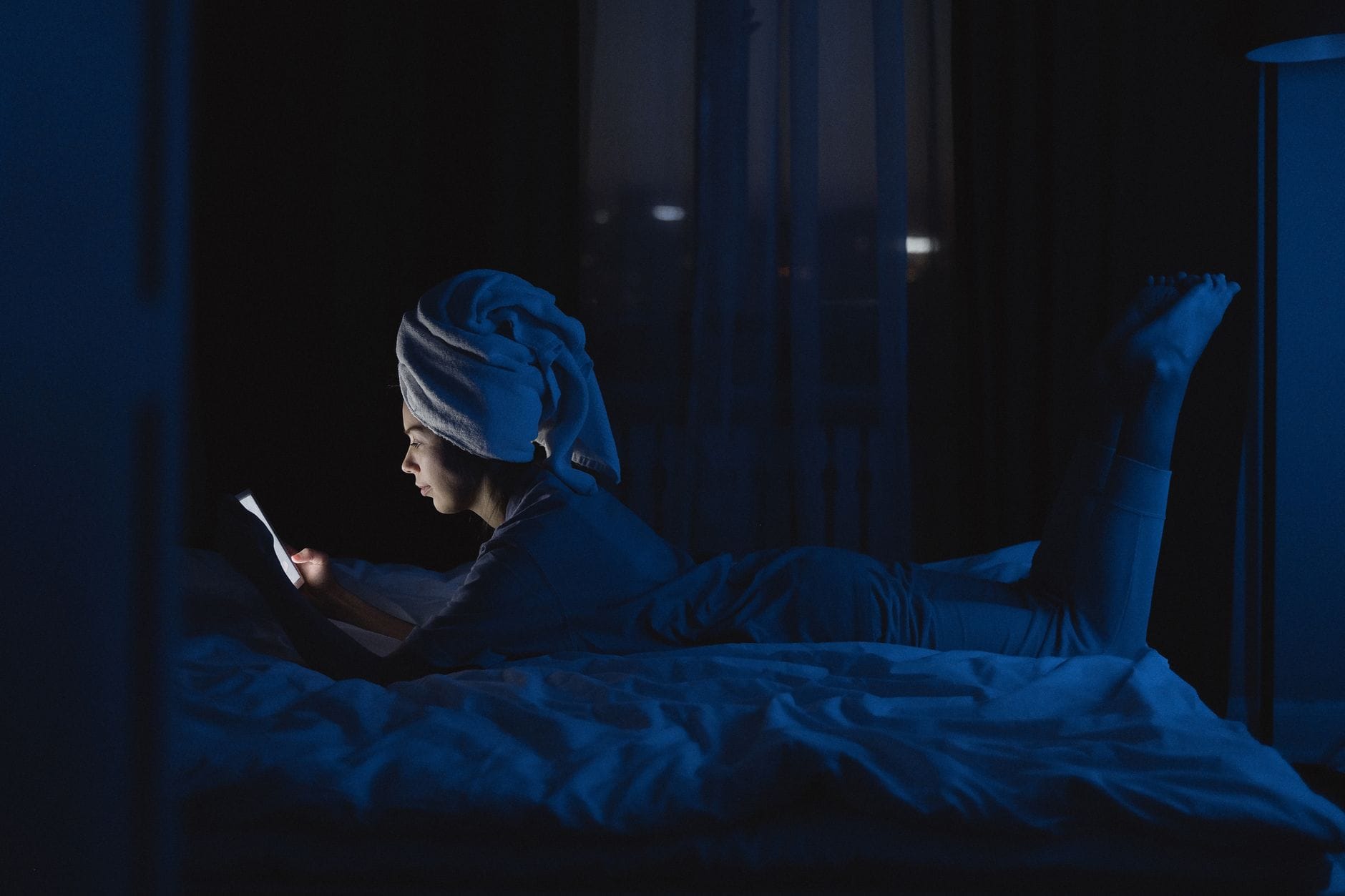 Kobieta w łóżku z ręcznikiem na głowie przegląda telefon nocą