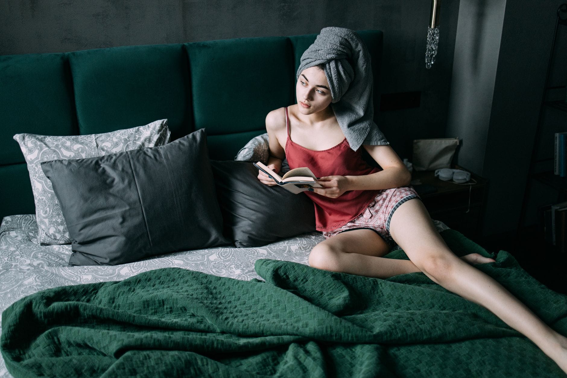 Kobieta z turbanem z ręcznika czyta książkę na łóżku w sypialni