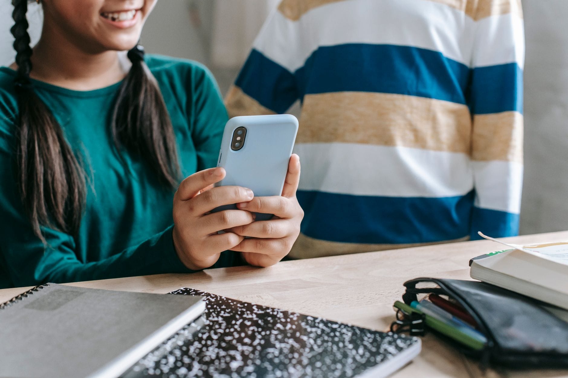 Uśmiechnięta uczennica w klasie pokazuje koleżance coś na smartfonie Uśmiechnięta uczennica w klasie pokazuje koleżance coś na smartfonie